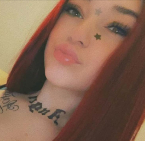 Close-up selfie-style photo of a young woman with long red hair, star stickers on her face, and a neck tattoo.